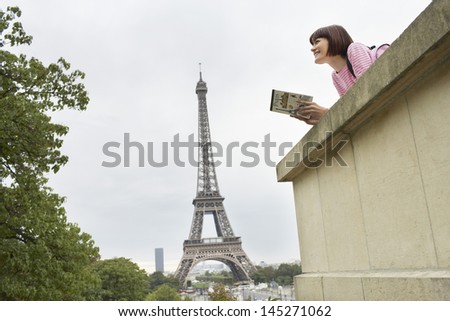 Low angle view of a young woman with book on balcony against Eiffel Tower