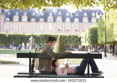Relaxed young couple reading book on city park bench