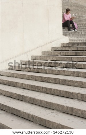 Young woman reading book while sitting on steps