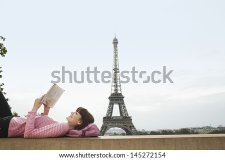 Side view of a young woman lying on balcony and reading book in front of Eiffel Tower Side view of a young woman lying on balcony and reading book in front of Eiffel Tower