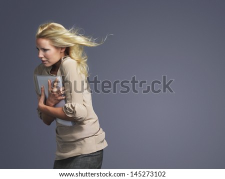 Side view of a young businesswoman with folder and blond hair blowing in wind against gray background