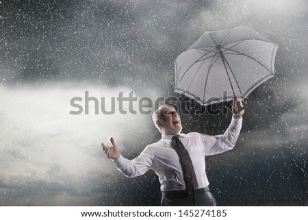 Low angle view of a middle aged businessman with umbrella laughing in storm