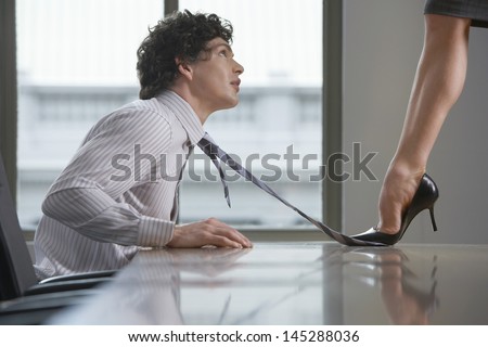 Side view of a highheeld businesswoman stepping on businessman\'s tie on desk