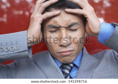 Closeup of a stressed businessman holding head in hands with eyes closed