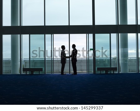 Side view of two silhouette businessmen shaking hands in the airport lobby