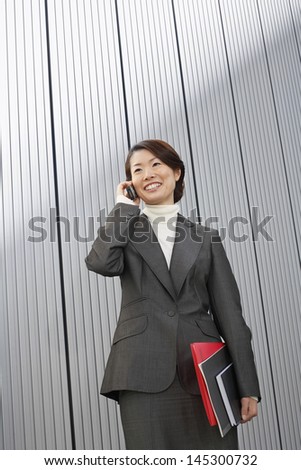 Smiling young businesswoman with folders using cellphone