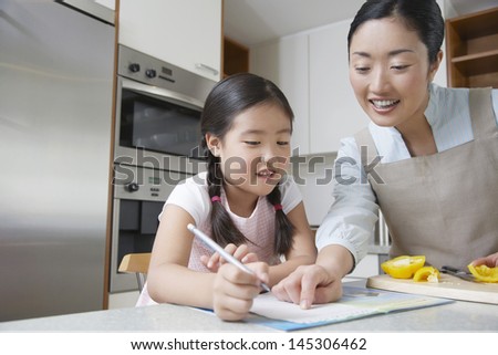 Mother assisting girl with her homework in the kitchen