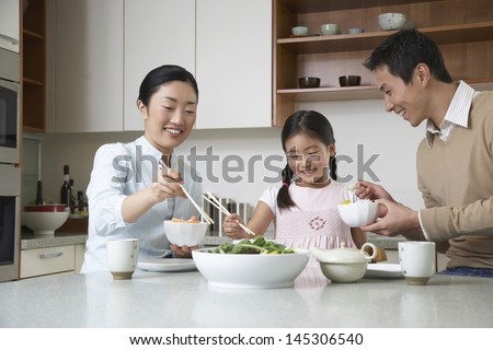 Young couple and daughter eating meal with chopsticks on kitchen counter