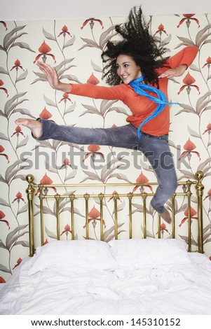 Full length of a smiling teenage girl jumping on bed