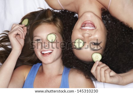 Overhead view of two teenage girls lying pink sheet with cucumbers over eyes
