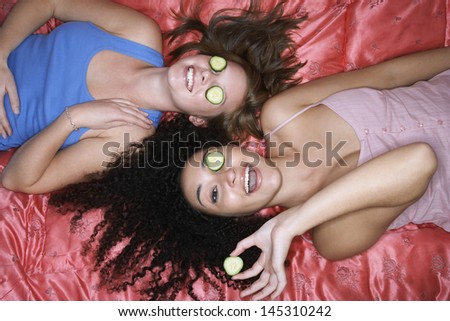Overhead view of two teenage girls lying pink sheet with cucumbers over eyes