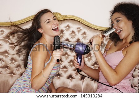 Teenage girls playing with brushes and hair dryer at slumber party