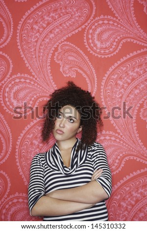 Teenage girl with arms crossed in striped top standing against colorful wallpaper