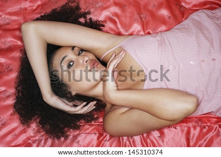 Overhead view of a teenage girl lying on pink sheet and puckering lips