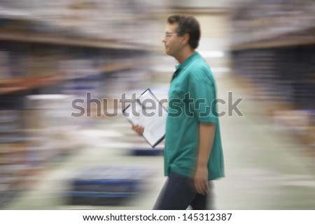 Side view of a warehouse worker walking with a clipboard