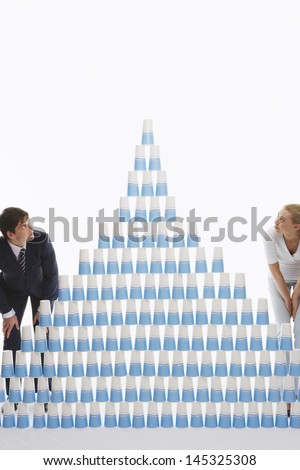 Man and woman admiring pyramid of stacked plastic cups against white background