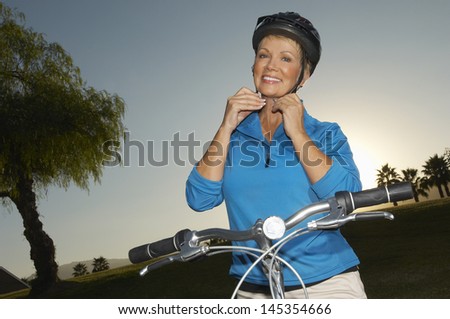 Senior woman adjusting cycling helmet at dusk portrait
