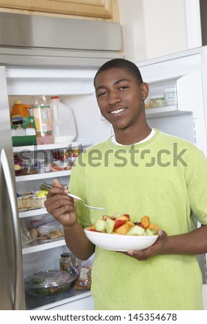 Young man eating salad by open fridge