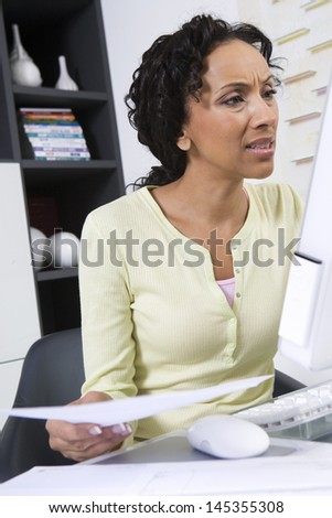 Tensed African American woman with document looking at computer screen