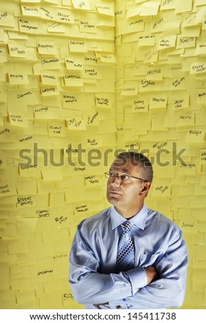 Middle aged businessman standing in front of wall covered in sticky notes