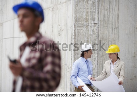 Managers with blueprint and blurred worker in foreground at construction site