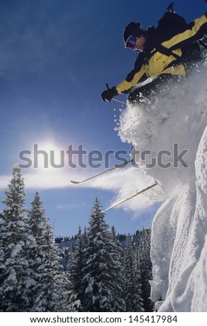 Low angle view of a skier jumping from snow bank through snow