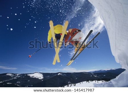 Low angle view of two skiers launching off snow bank hitting the slopes