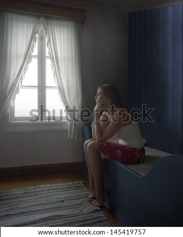 Side view of a young thoughtful and sad woman sitting alone in room