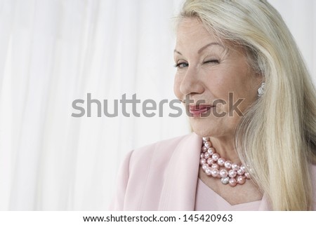 Closeup of a happy and glamorous senior woman winking against white background