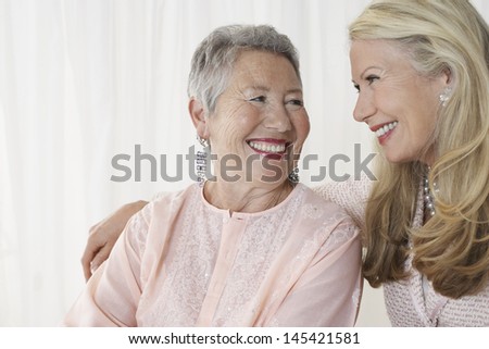 Two happy elegant senior women looking at each other against white background