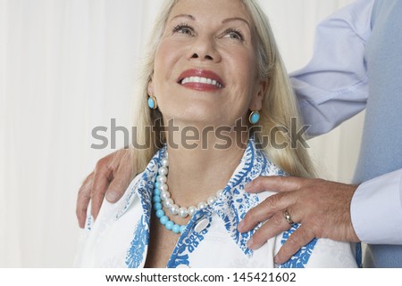 Closeup of a smiling senior woman with man\'s hands on shoulders against white background