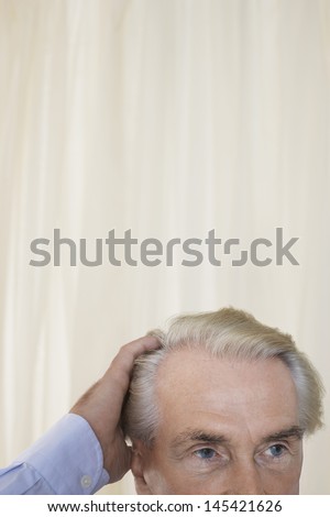Closeup high section of a senior man with hand in hair against curtain