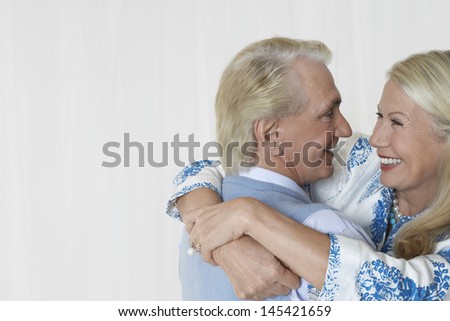 Side view of a loving and happy senior couple embracing against white background