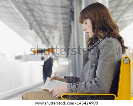 Side View Of A Businesswoman Reading A Book At Train Station Bench