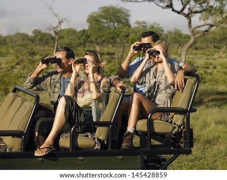 Group of tourists sitting in jeep and looking through binoculars