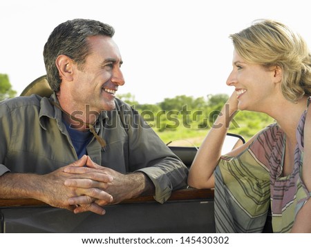 Closeup side view of a man and woman talking by jeep against clear sky