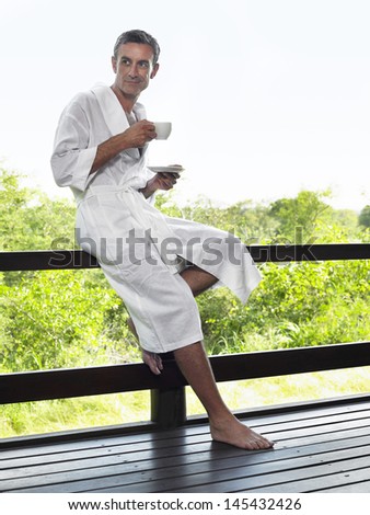 Full length of a man in bathrobe on terrace railing with tea cup