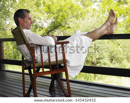Full length side view of a man in bathrobe sitting on chair in terrace with feet up