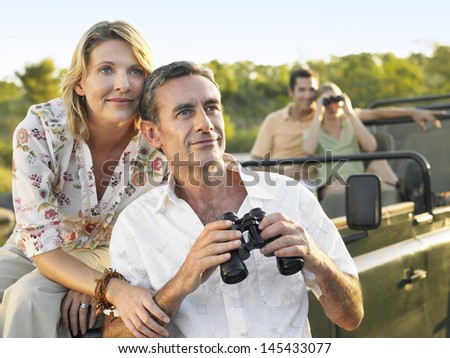 Two happy couples on trip with binoculars in jeep