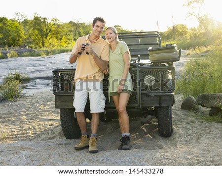 Full length of a smiling young couple standing by jeep with binoculars