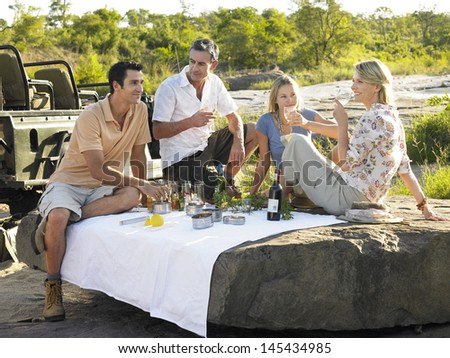Four people enjoying picnic on rock with trees in background