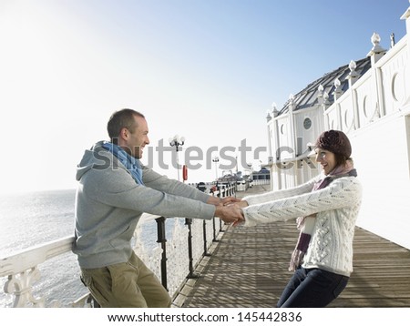 Side view of a couple holding hands and spinning around on pier by sea