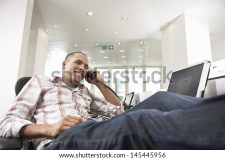 Casually dressed happy mixed race businessman with feet on desk talking on phone