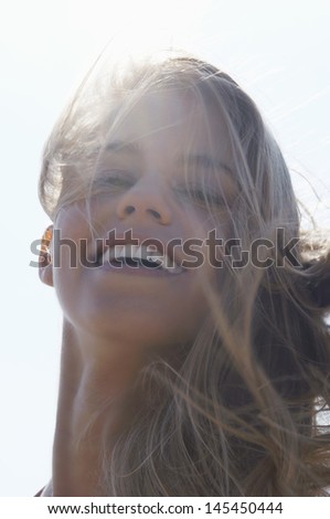 Closeup portrait of a cheerful young woman with windy hair against the sky