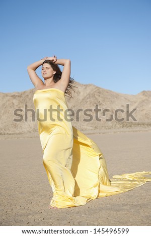 Young woman wrapped in yellow cloth on arid landscape