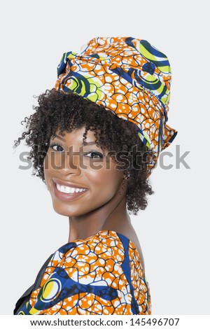 Portrait of young woman in African print attire looking over shoulder against gray background