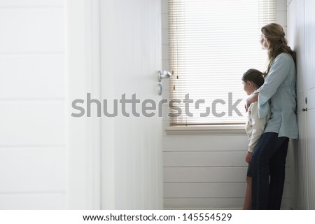 Side view of mother and daughter looking out of window blinds