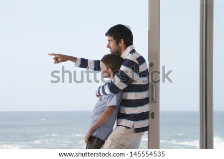 Side view of young boy with father pointing out to sea in doorway