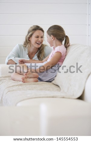 Cheerful mother crouching next to girl sitting on sofa at home