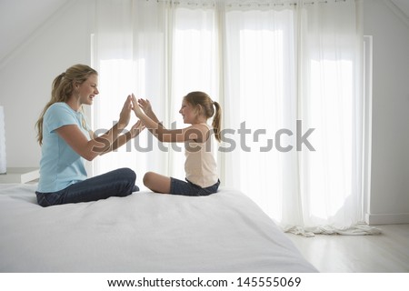Side View Of Happy Mother And Daughter Playing Patty-Cake On Bed